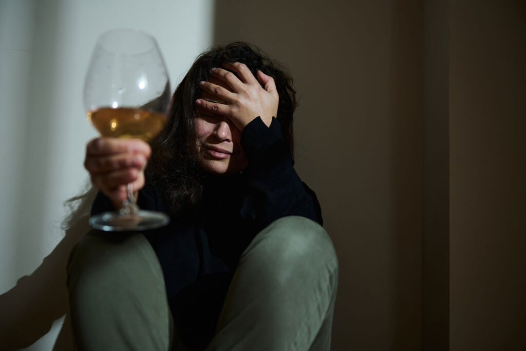 A seated individual holds a glass of wine with a somber and reflective expression